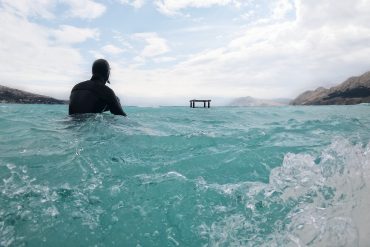 Surfing in wetsuit sitting on surfboard